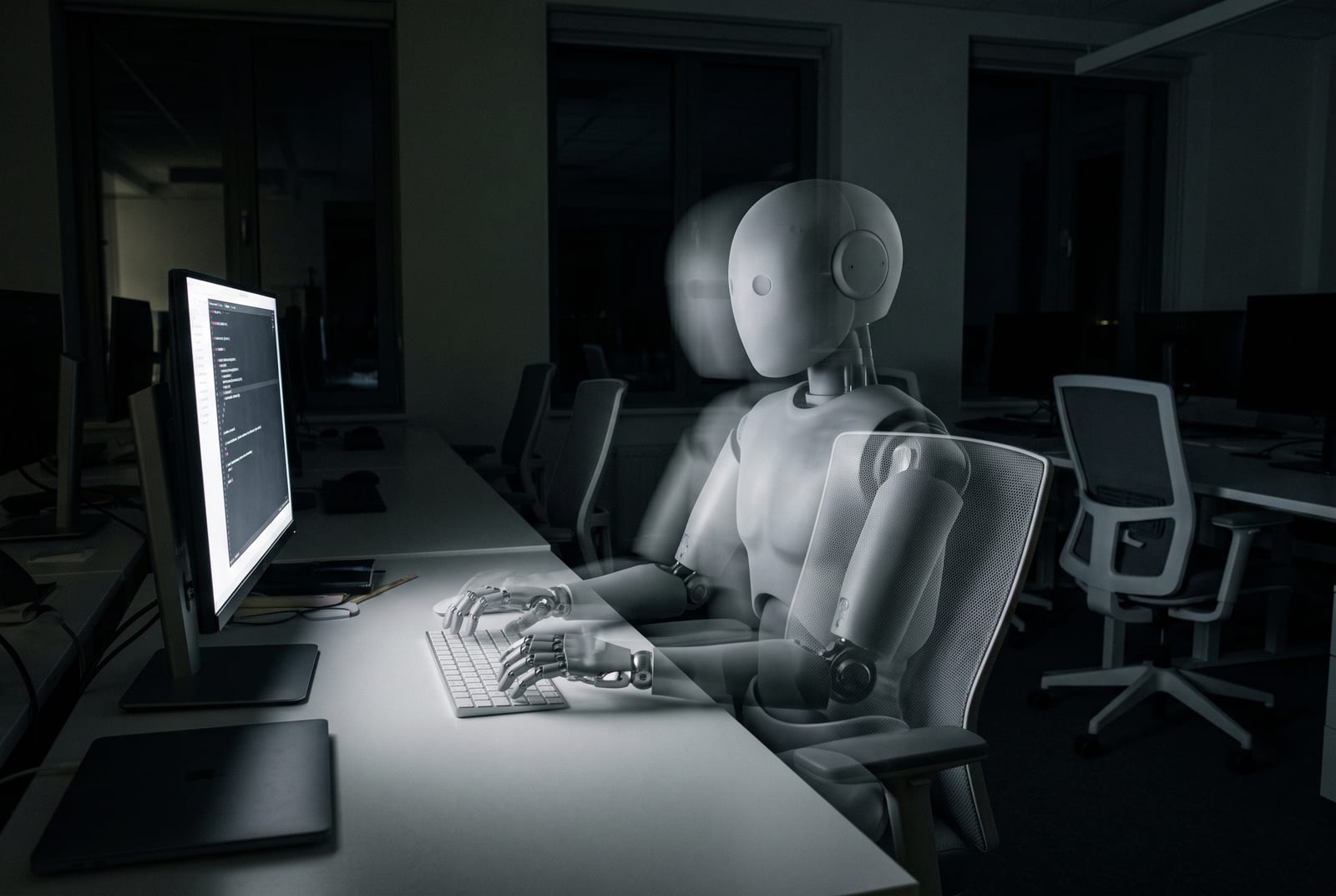 Un robot humanoide translúcido, como un fantasma, sentado en un puesto de trabajo en una oficina oscura de noche, con las manos en el teclado y la silla visible a través de su cuerpo.